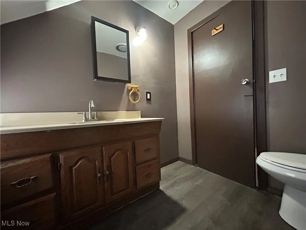 Half bathroom featuring vanity, toilet, wood finished floors, and baseboards