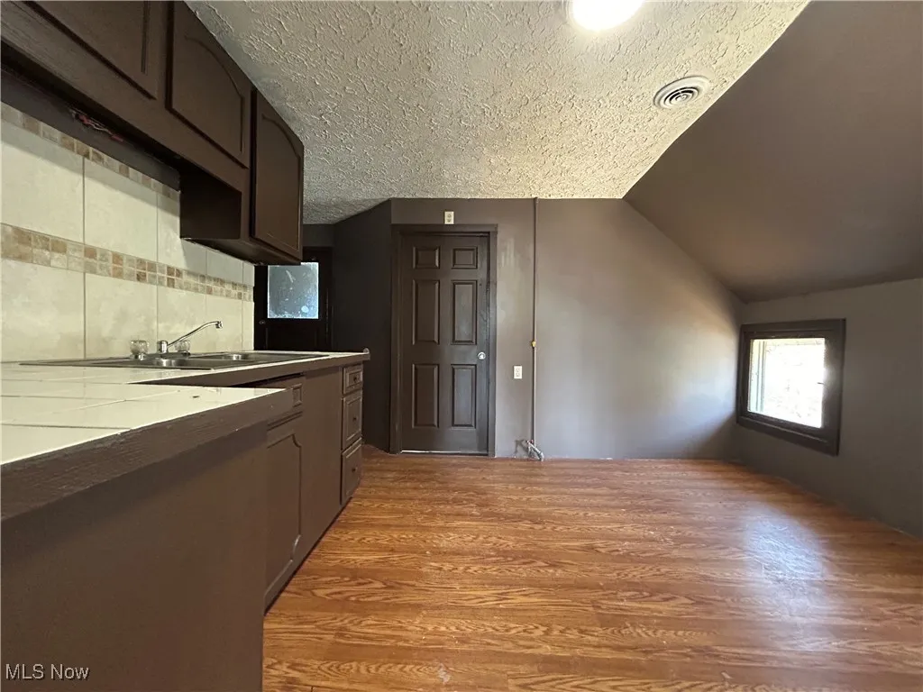 Kitchen featuring light wood-type flooring, lofted ceiling, decorative backsplash, a textured ceiling, and a sink