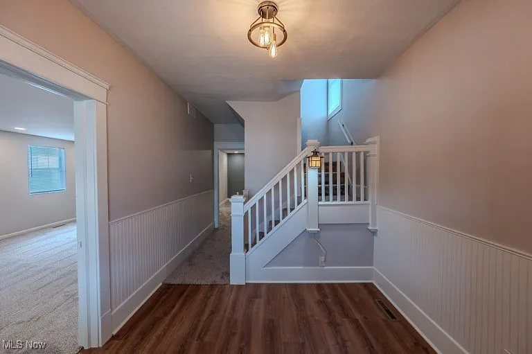 Entry way with Staircase featuring wood finished floors, visible vents, and wainscoting
