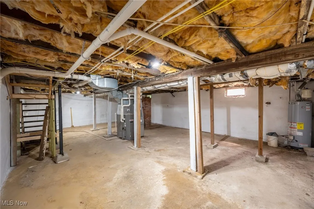 Basement with gas water heater, heating unit, and stairs