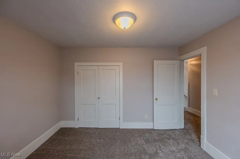 Unfurnished bedroom featuring baseboards, a closet, dark carpet, and a textured ceiling