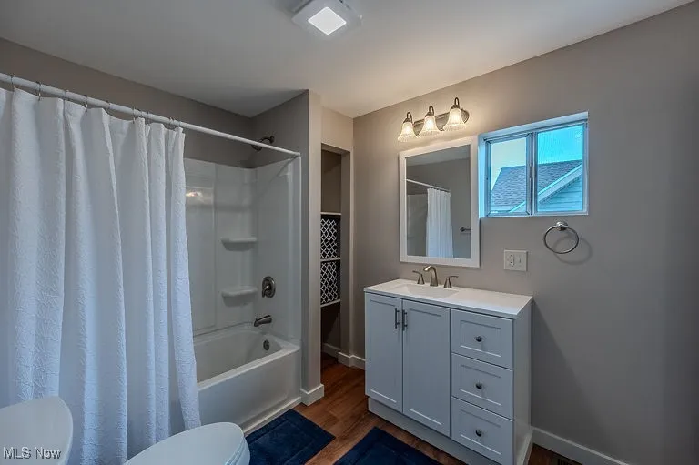 Full bath with vanity, wood finished floors, baseboards, shower / bath combo with shower curtain, and toilet