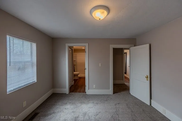 Unfurnished bedroom featuring connected bathroom, baseboards, and carpet floors