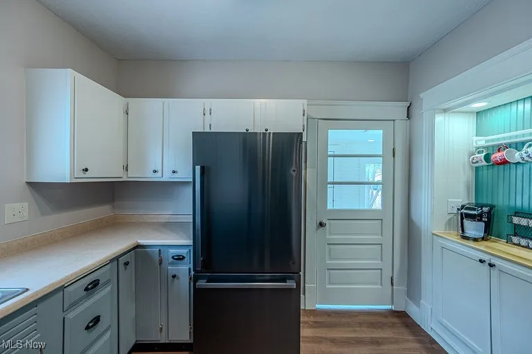 Kitchen with white cabinetry, light countertops, freestanding refrigerator, and dark wood-style flooring