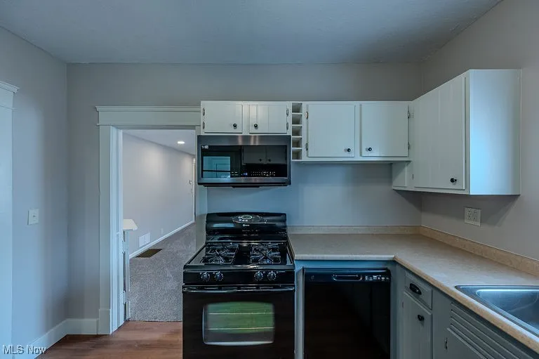 Kitchen featuring black appliances, dark wood-style floors, white cabinets, light countertops, and baseboards