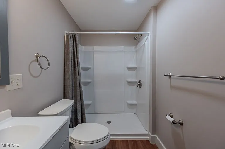 Bathroom featuring toilet, curtained shower, wood finished floors, baseboards, and vanity