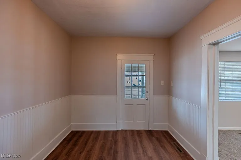 Doorway to outside from featuring dark wood-style floors and a wainscoted wall