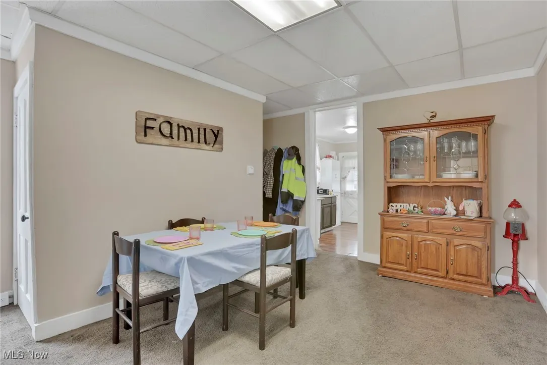 Dining space with baseboards, a paneled ceiling, light colored carpet, and crown molding