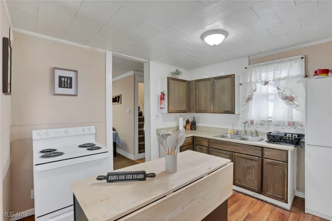 Kitchen with white appliances, crown molding, light wood-type flooring, and a sink