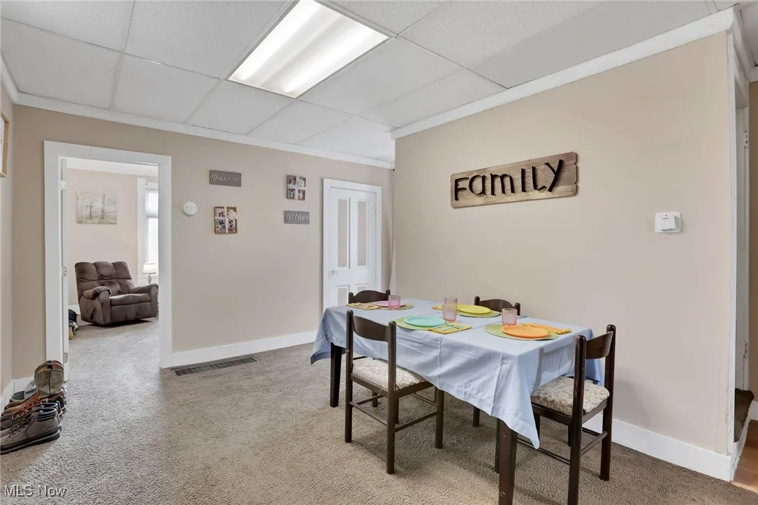 Carpeted dining area with visible vents, a paneled ceiling, and baseboards