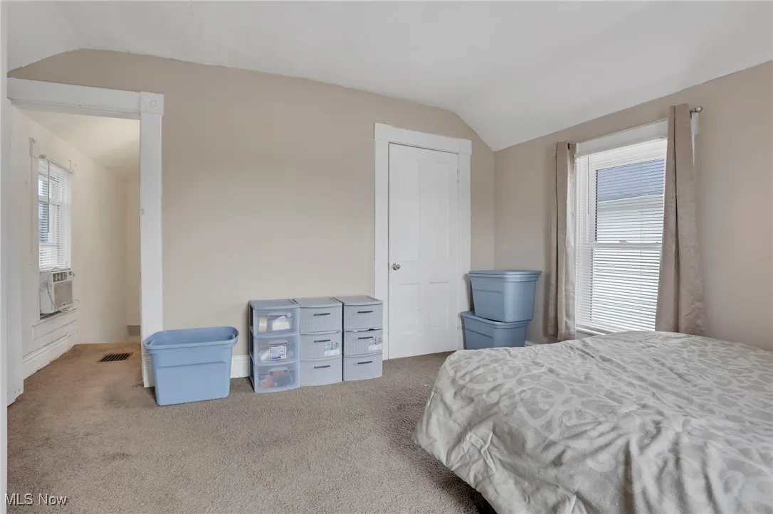 Bedroom with vaulted ceiling, carpet flooring, cooling unit, and visible vents