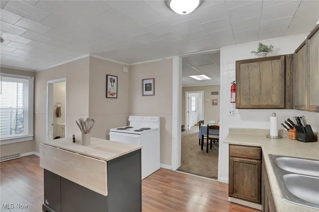 Kitchen with crown molding, light countertops, light wood-style floors, and white electric range oven