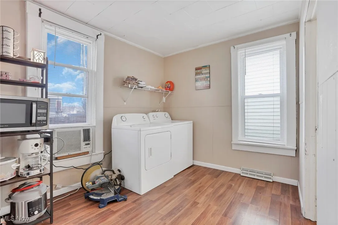 Clothes washing area featuring light wood-type flooring, visible vents, ornamental molding, separate washer and dryer, and baseboards