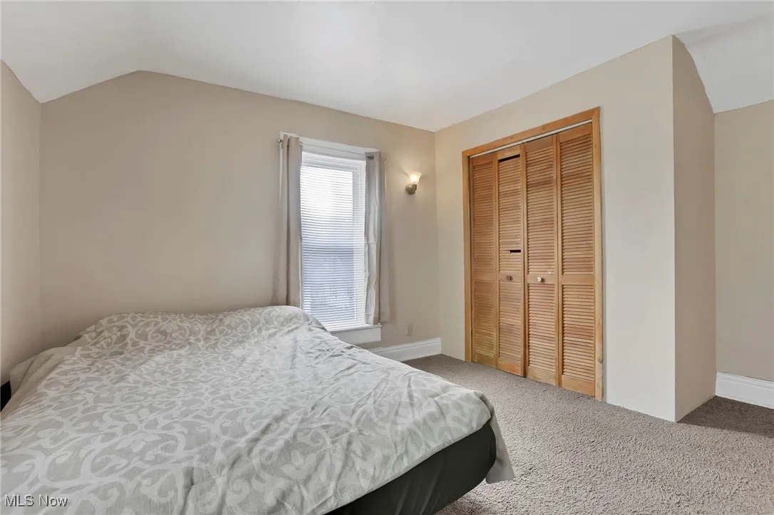 Carpeted bedroom with a closet, lofted ceiling, and baseboards