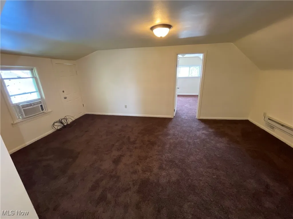 Bonus room with lofted ceiling, dark colored carpet, and cooling unit
