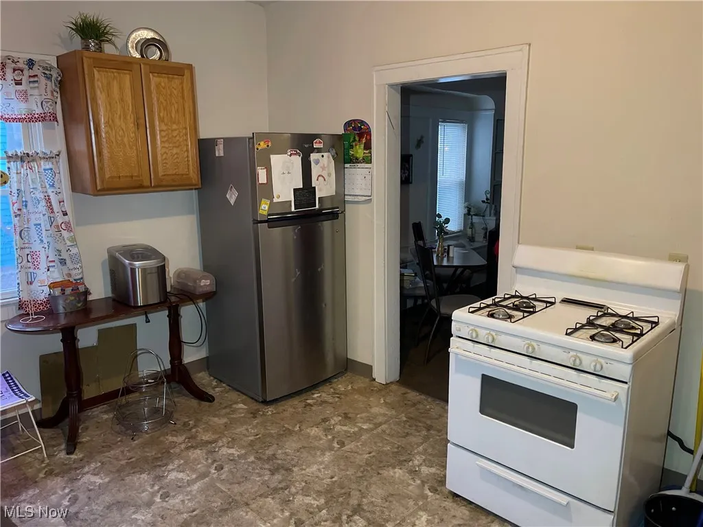 Kitchen featuring white gas range, brown cabinetry, and freestanding refrigerator