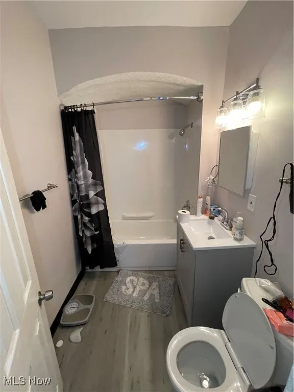 Bathroom featuring toilet, wood finished floors, vanity, and shower / bathtub combination with curtain