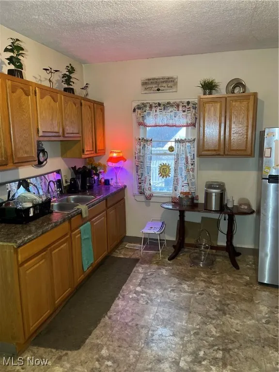 Kitchen featuring refrigerator, brown cabinetry, baseboards, and a sink
