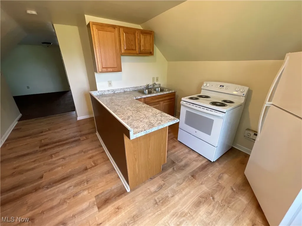 Kitchen featuring white appliances, lofted ceiling, light wood-type flooring, light countertops, and a peninsula