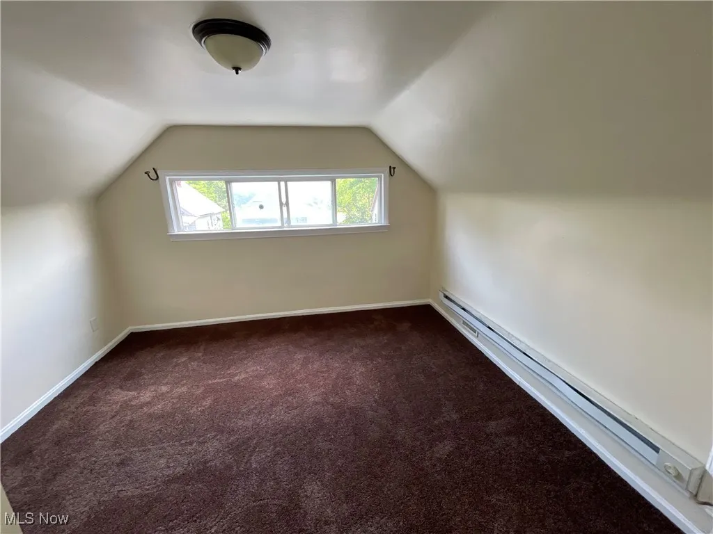 Additional living space with dark colored carpet, a baseboard heating unit, and vaulted ceiling