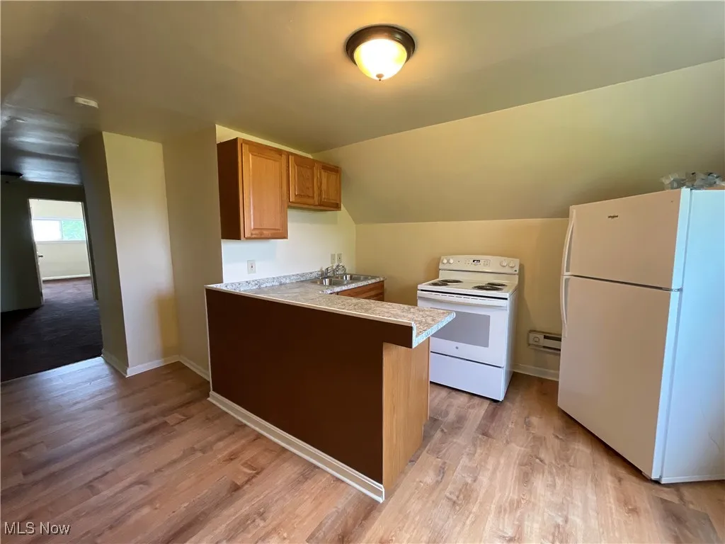 Kitchen with white appliances, a peninsula, light wood-type flooring, light countertops, and vaulted ceiling