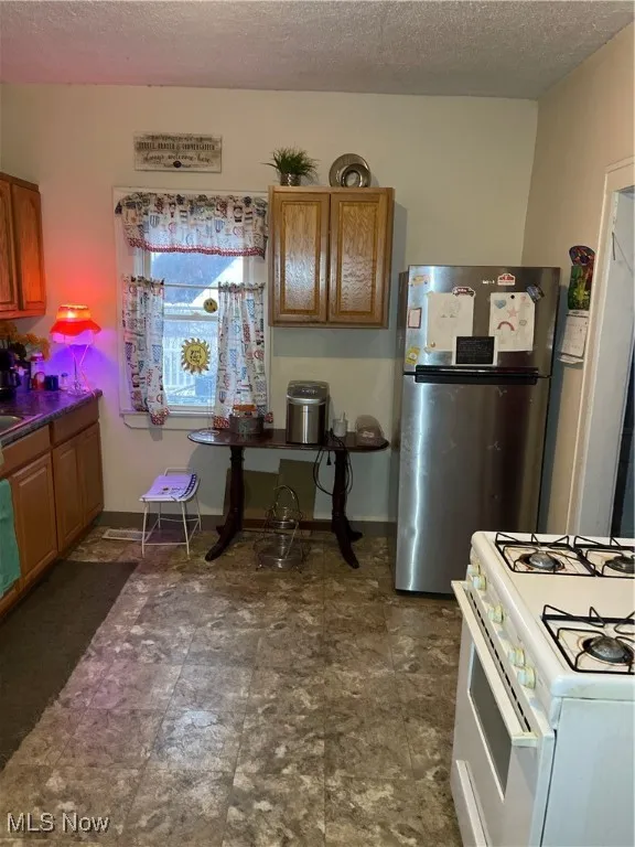 Kitchen featuring fridge, brown cabinetry, stove, and a textured ceiling