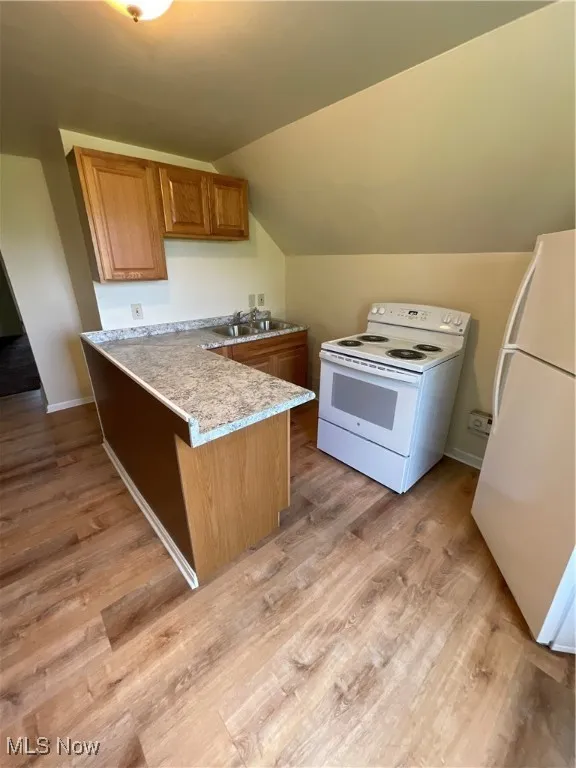 Kitchen featuring range, fridge, a peninsula, vaulted ceiling, and light countertops