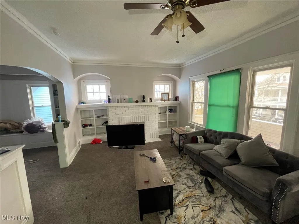 Living room with baseboards, ornamental molding, carpet floors, a fireplace, and a textured ceiling