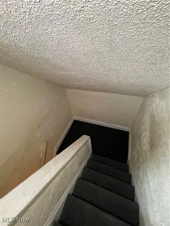 Stairway featuring vaulted ceiling, a textured wall, and a textured ceiling