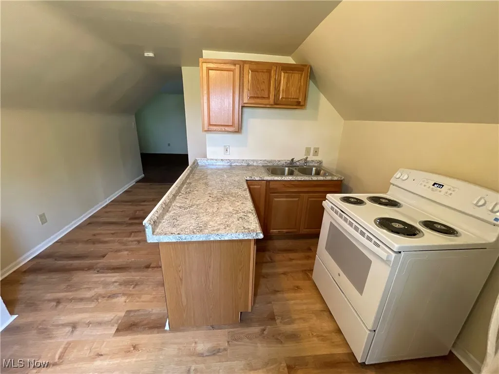 Kitchen featuring electric stove, light countertops, lofted ceiling, light wood-type flooring, and a peninsula