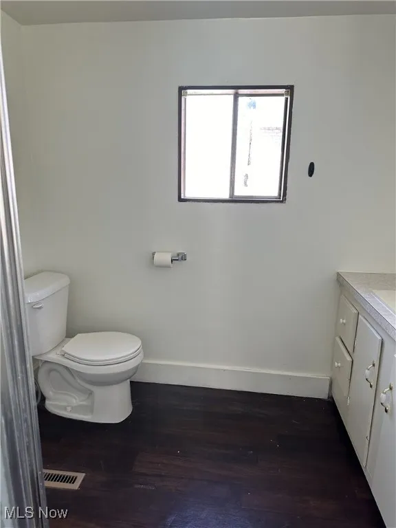 Half bath with vanity, wood finished floors, visible vents, baseboards, and toilet