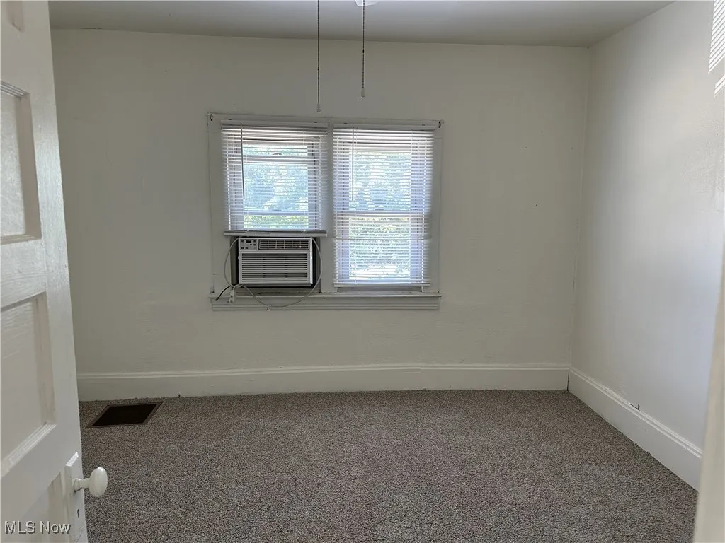 Carpeted empty room featuring visible vents, baseboards, and cooling unit