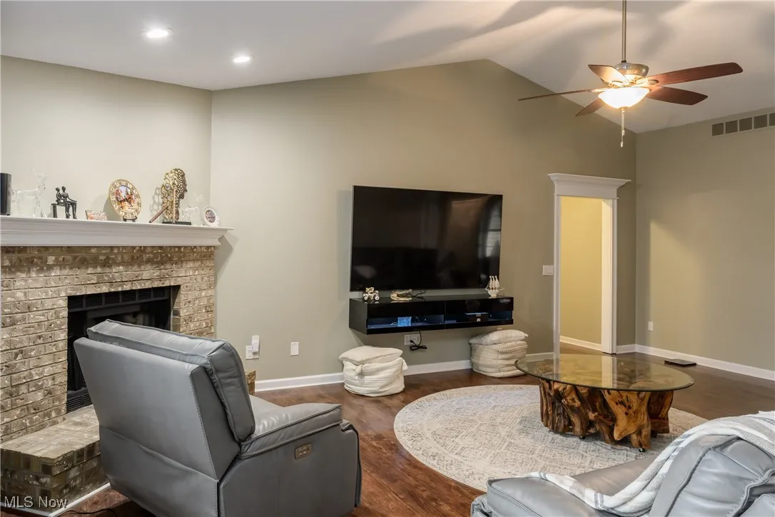 Living room featuring visible vents, a brick fireplace, baseboards, lofted ceiling, and wood finished floors