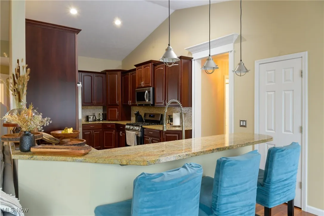 Kitchen featuring stainless steel appliances, lofted ceiling, tasteful backsplash, and a breakfast bar area