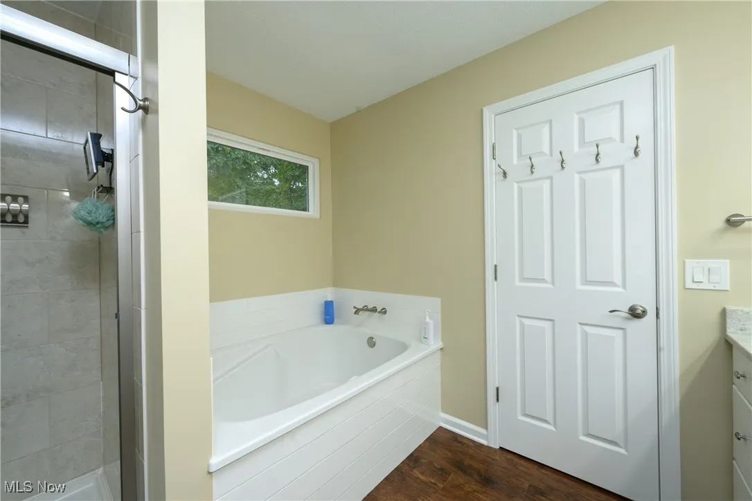 Full bath with a garden tub, wood finished floors, vanity, and a tile shower