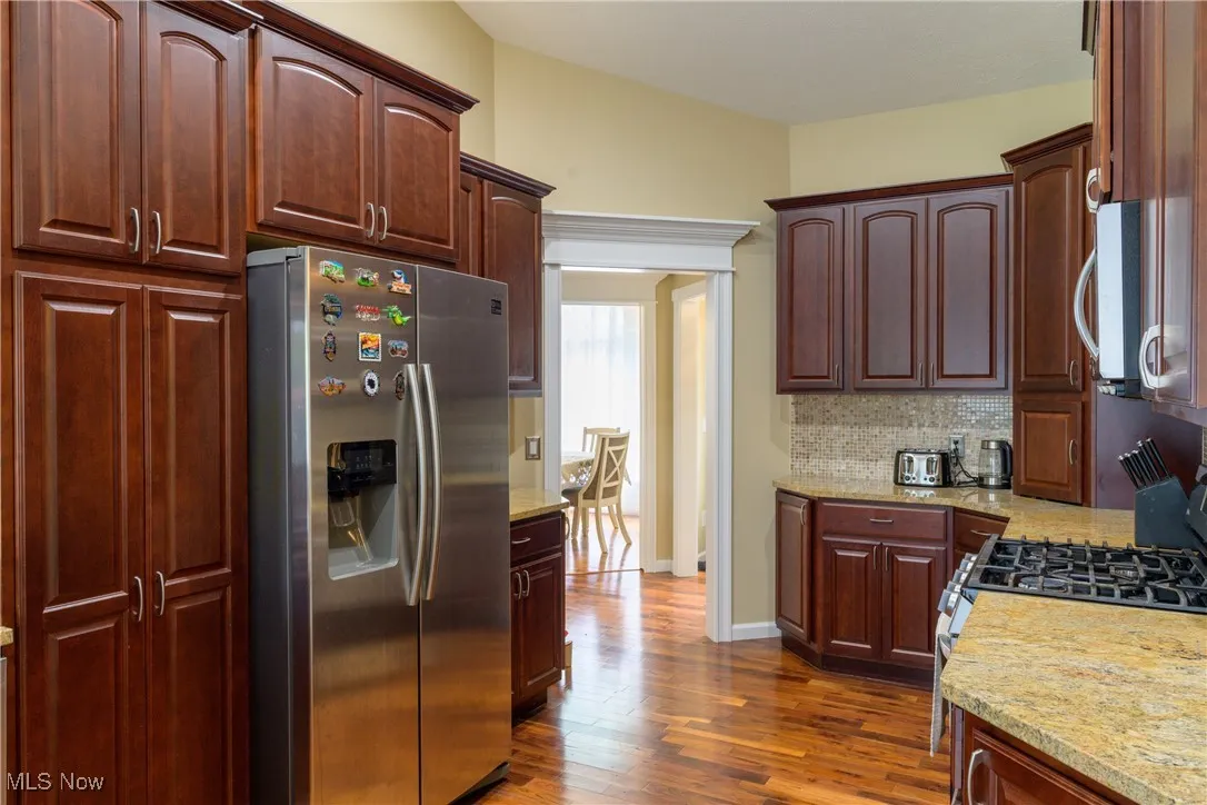 Kitchen with backsplash, dark wood-type flooring, baseboards, light stone counters, and appliances with stainless steel finishes