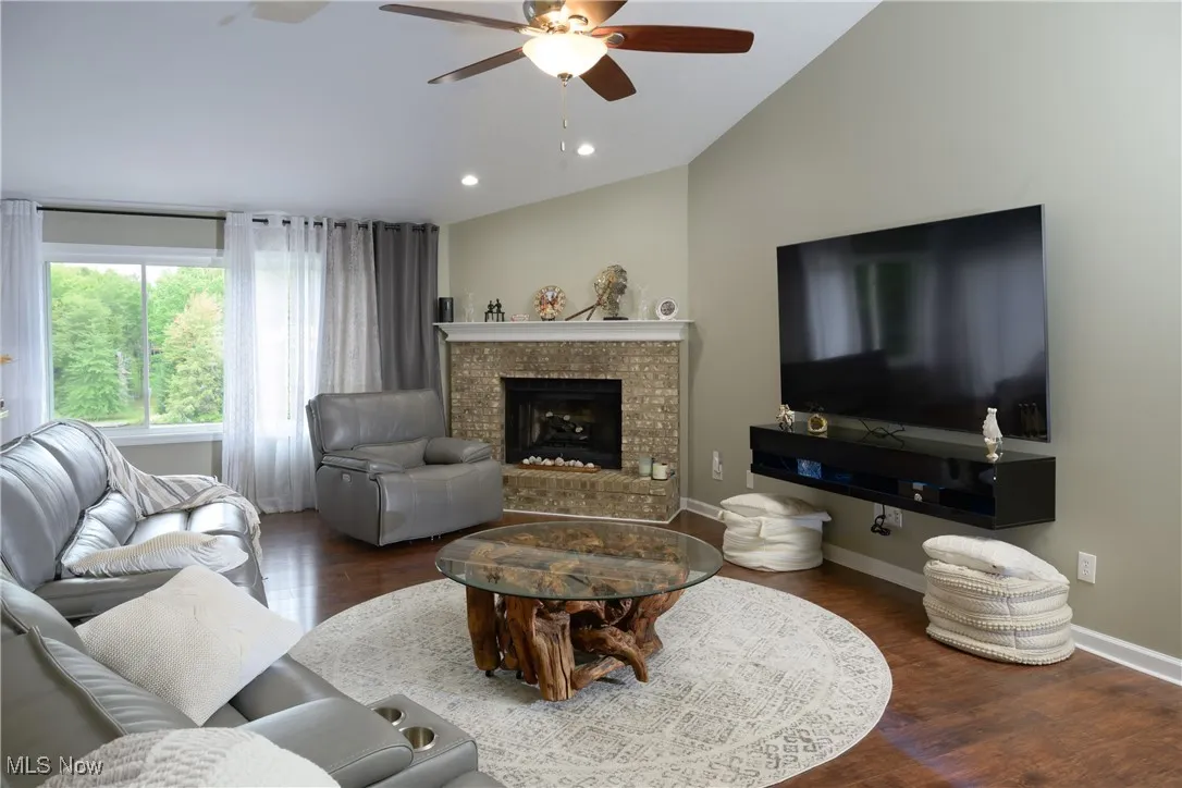 Living room with lofted ceiling, wood finished floors, baseboards, and ceiling fan