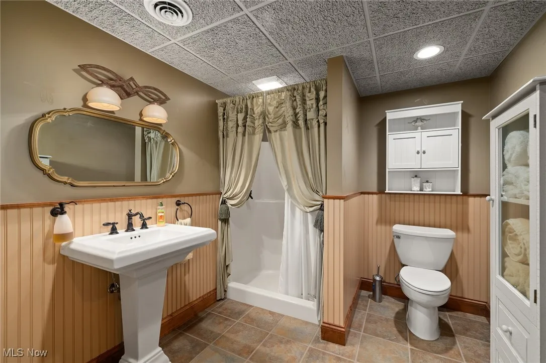 Full bath with visible vents, toilet, a stall shower, a drop ceiling, and wainscoting