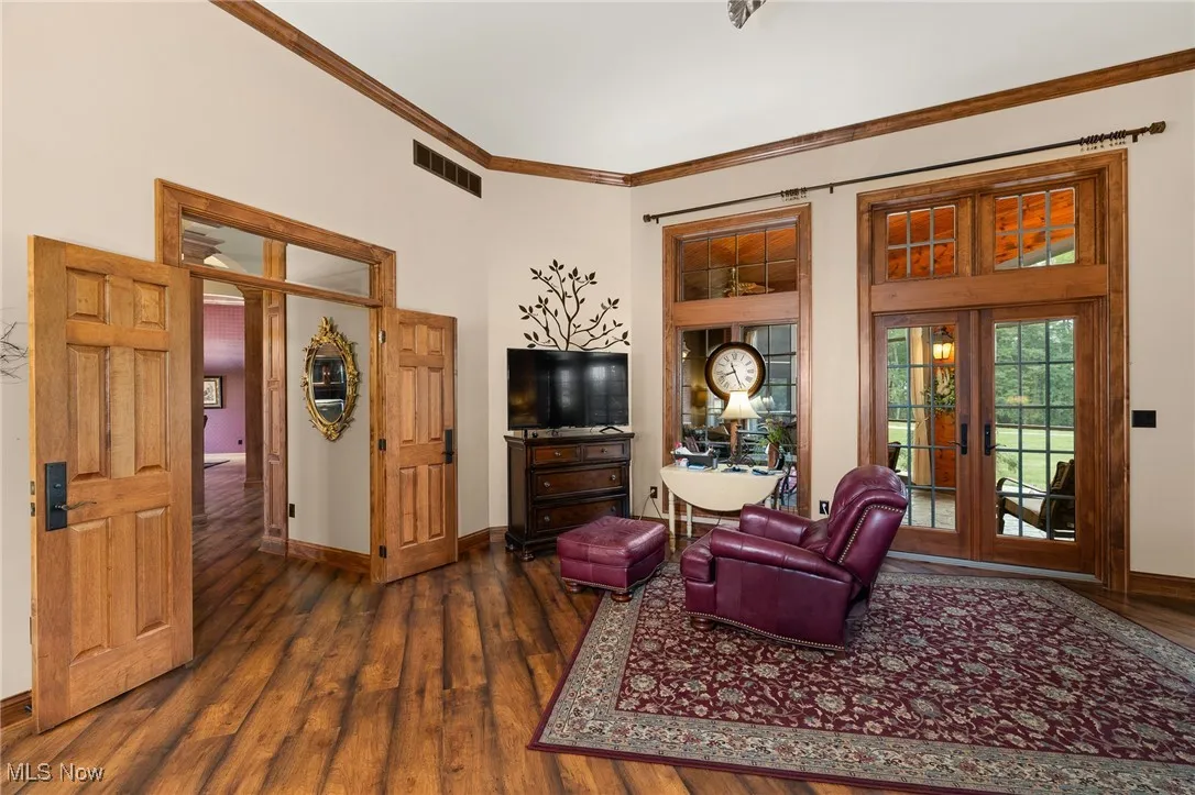 Living area with dark wood-style floors, visible vents, baseboards, french doors, and crown molding