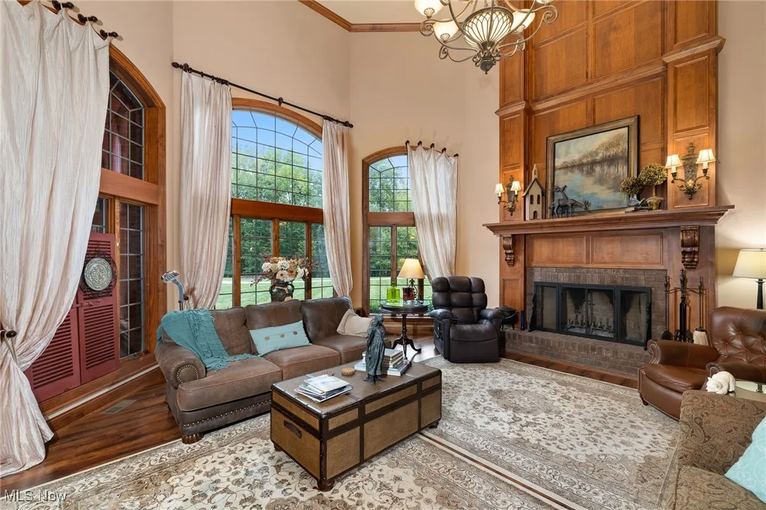 Living area with a notable chandelier, ornamental molding, wood finished floors, a brick fireplace, and a towering ceiling