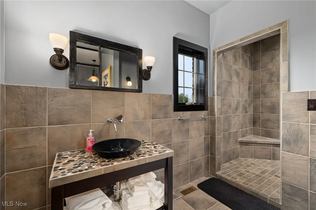 Bathroom featuring a wainscoted wall, tiled shower, tile walls, and a sink