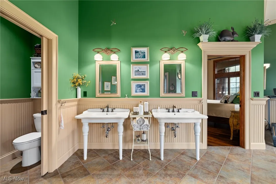 Ensuite bathroom featuring connected bathroom, toilet, and wainscoting