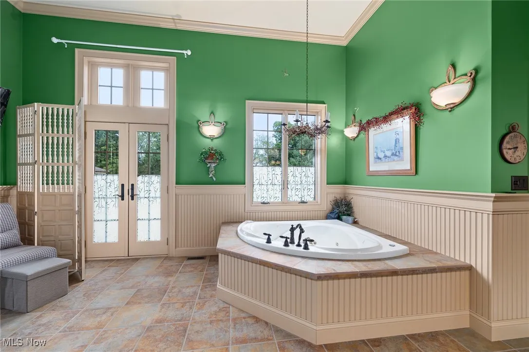 Bathroom featuring a wainscoted wall, an inviting chandelier, ornamental molding, french doors, and a bath