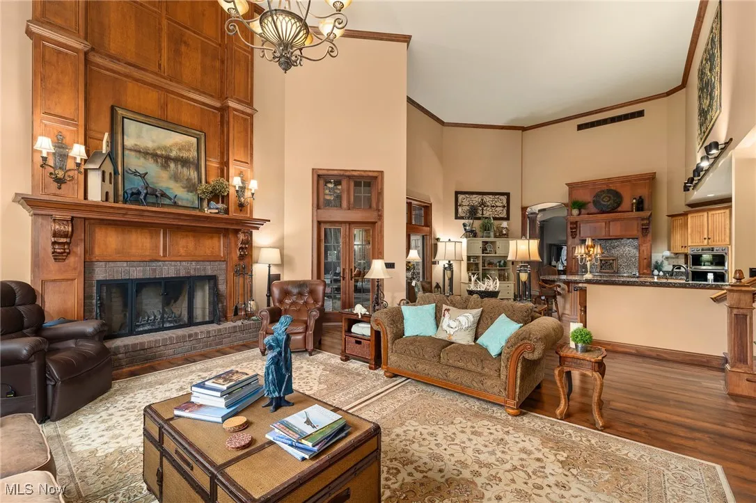 Living area with wood finished floors, an inviting chandelier, a high ceiling, a fireplace, and crown molding