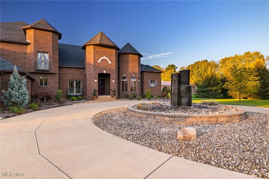 View of front of house featuring brick siding, curved driveway, and a shingled roof