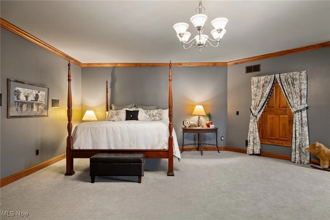 Bedroom with visible vents, crown molding, baseboards, carpet, and a notable chandelier