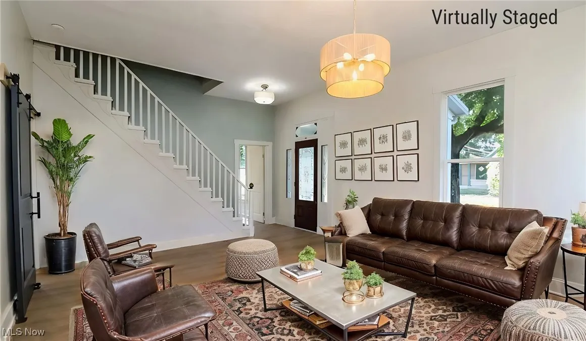 Living area featuring an inviting chandelier, stairs, baseboards, and wood finished floors. Virtually Staged.