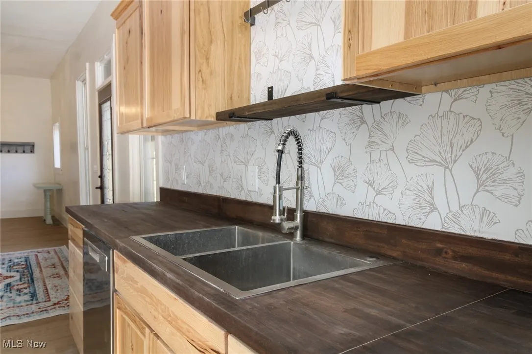 Kitchen featuring dark countertops, stainless steel dishwasher, light brown cabinetry, and a sink