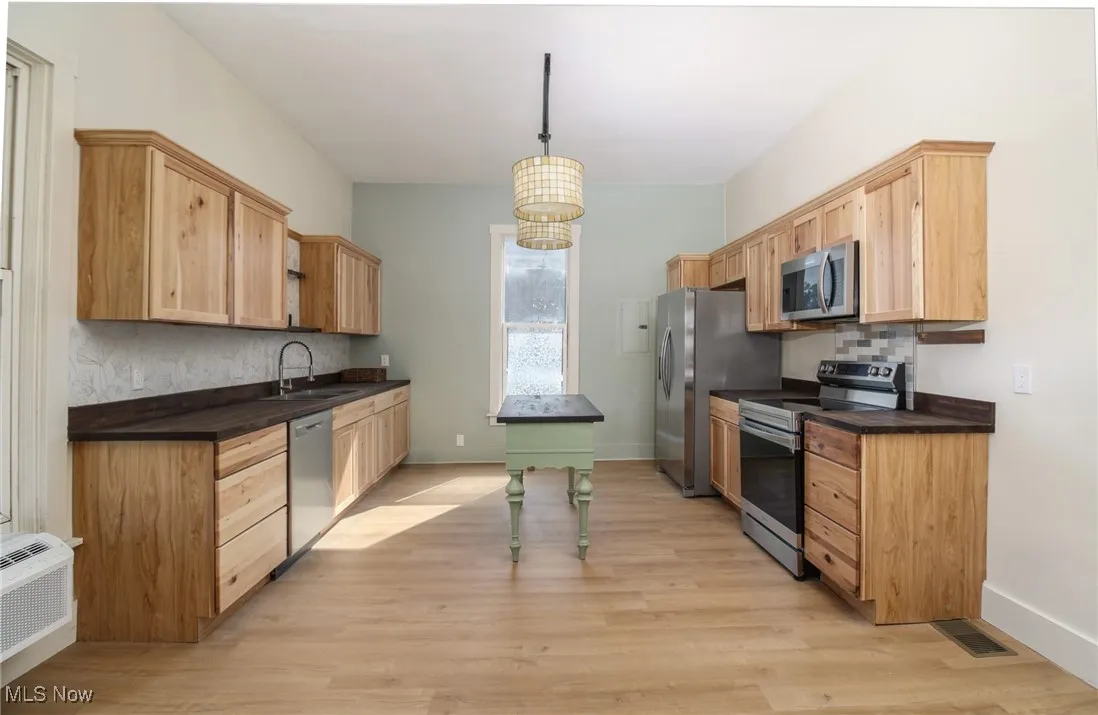 Kitchen with light wood finished floors, a sink, decorative backsplash, appliances with stainless steel finishes, and dark countertops