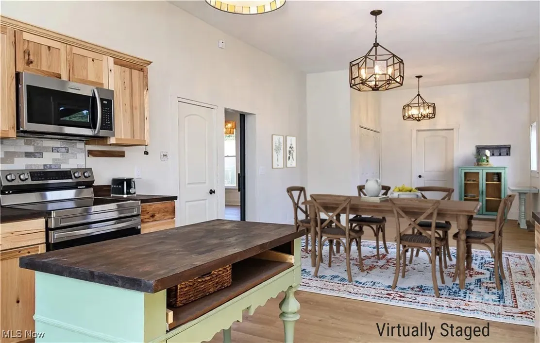 Kitchen featuring light brown cabinetry, decorative backsplash, wood finished floors, stainless steel appliances, and wood counter on kitchen island. Virtually Staged